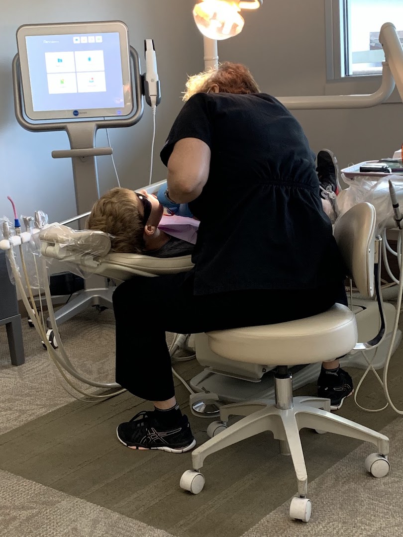 A dental professional treats a patient in a dental chair, suitable for an about or services section