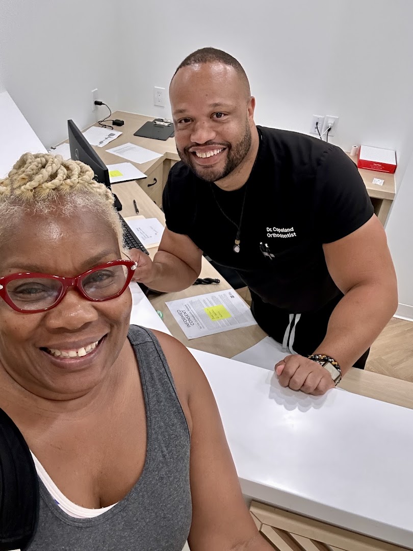 A smiling woman in red glasses with Dr. Copeland, Orthodontist, in the background
