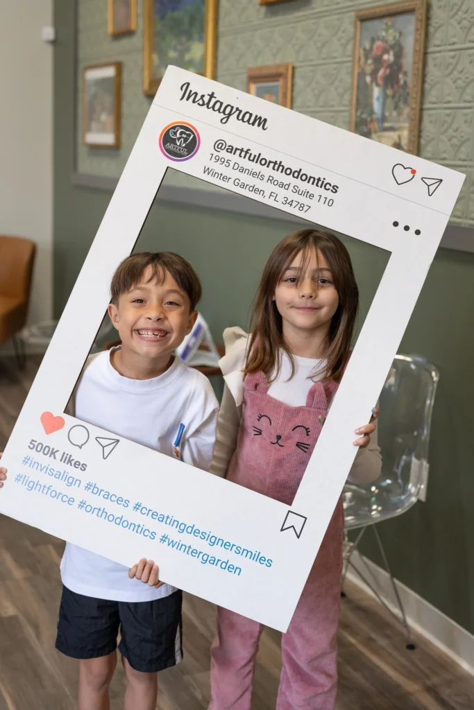 Two smiling children holding an Artful Orthodontics Instagram frame, showcasing patient happiness.