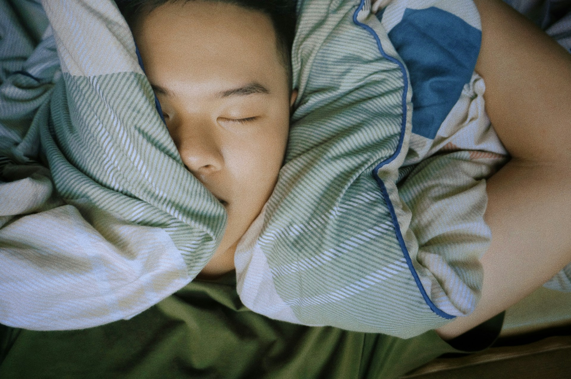 Close-up overhead shot of a person sleeping with their face nestled between striped green-and-white pillows, conveying deep restful sleep.