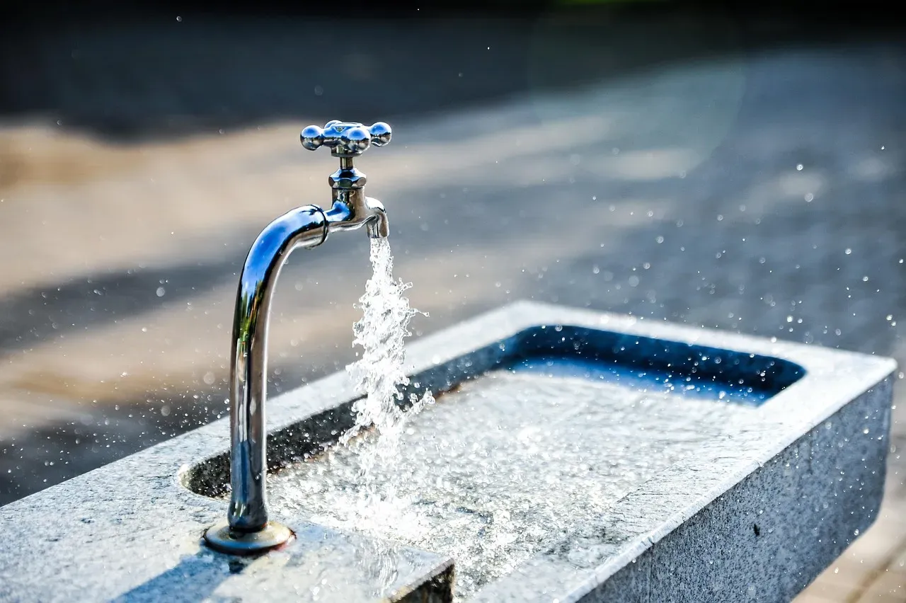 Chrome outdoor tap with water flowing forcefully into a granite basin, with a blurred street background