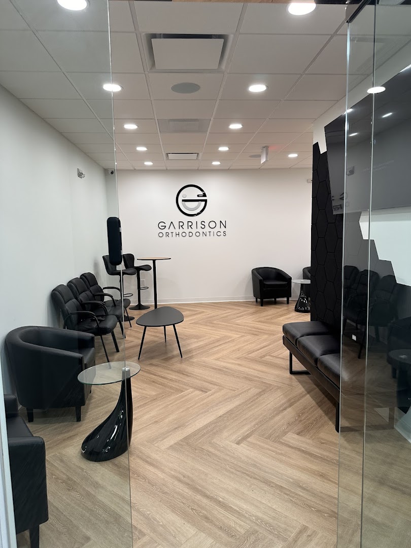 Modern orthodontic office waiting room with black leather seating, herringbone wood floors, and the Garrison Orthodontics logo mounted on the back wall. Clean, professional interior shot with good lighting and sharp detail.