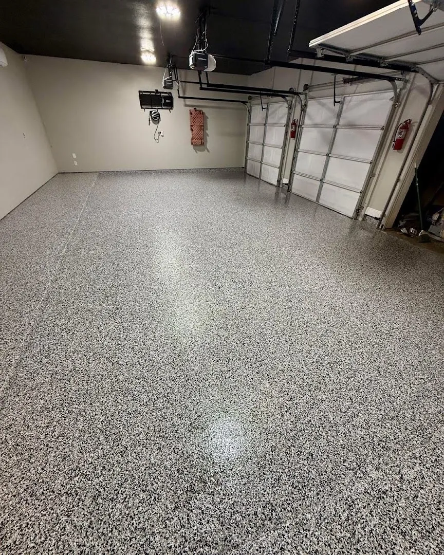 A clean two-car garage with a gray speckled flake epoxy floor coating, dark ceiling, and visible garage door openers and fire extinguisher.