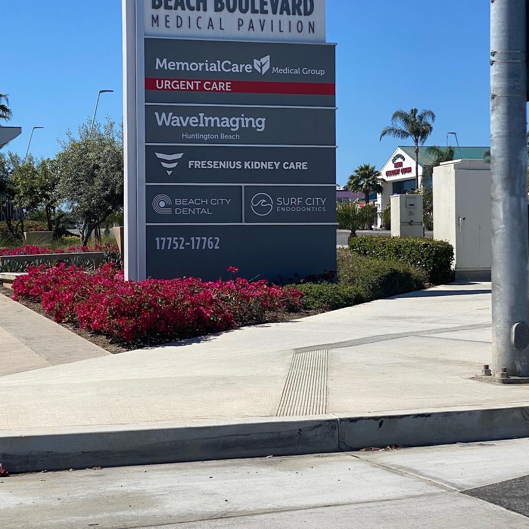 Outdoor medical pavilion directory sign reading 'Beach Boulevard Medical Pavilion' listing tenants including MemorialCare Urgent Care, WaveImaging, Fresenius Kidney Care, Beach City Dental, and Surf City Endodontics at address 17752-17762. Mid-quality smartphone photo with a utility pole partially obstructing the frame.