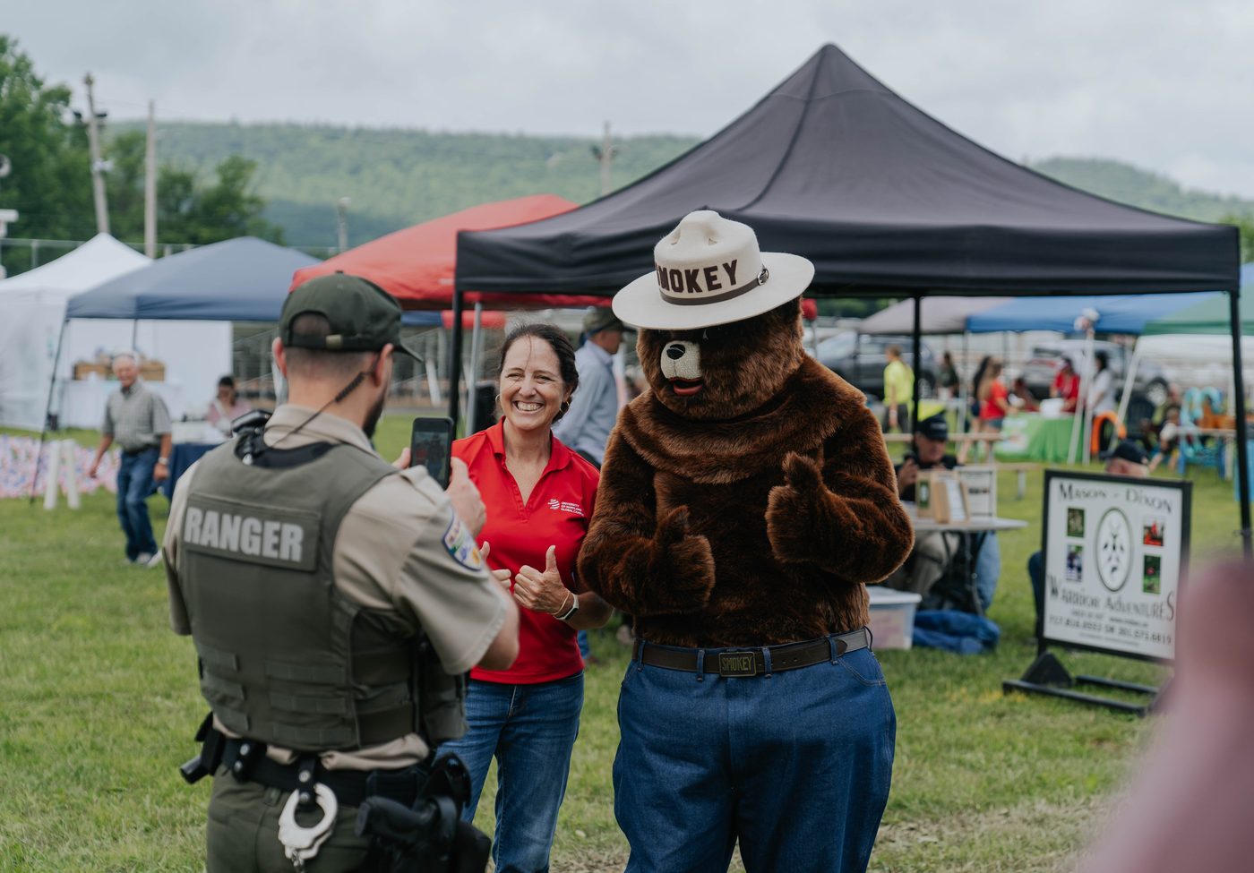 A ranger and a costumed mascot greeting guests at an event tent
