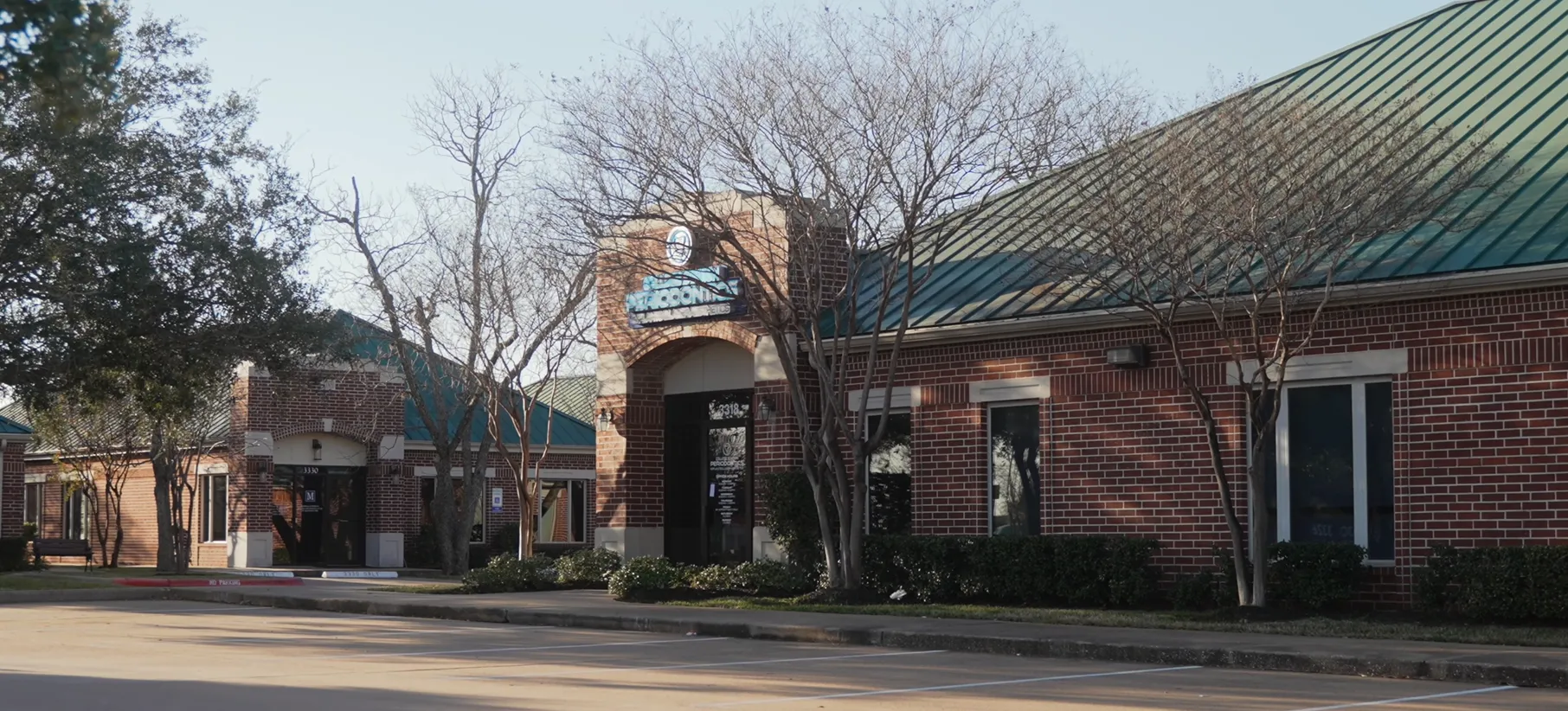 Wide-angle exterior shot of a brick office complex with green metal roofing, partially obscured signage reading 'McPherson Endodontics'